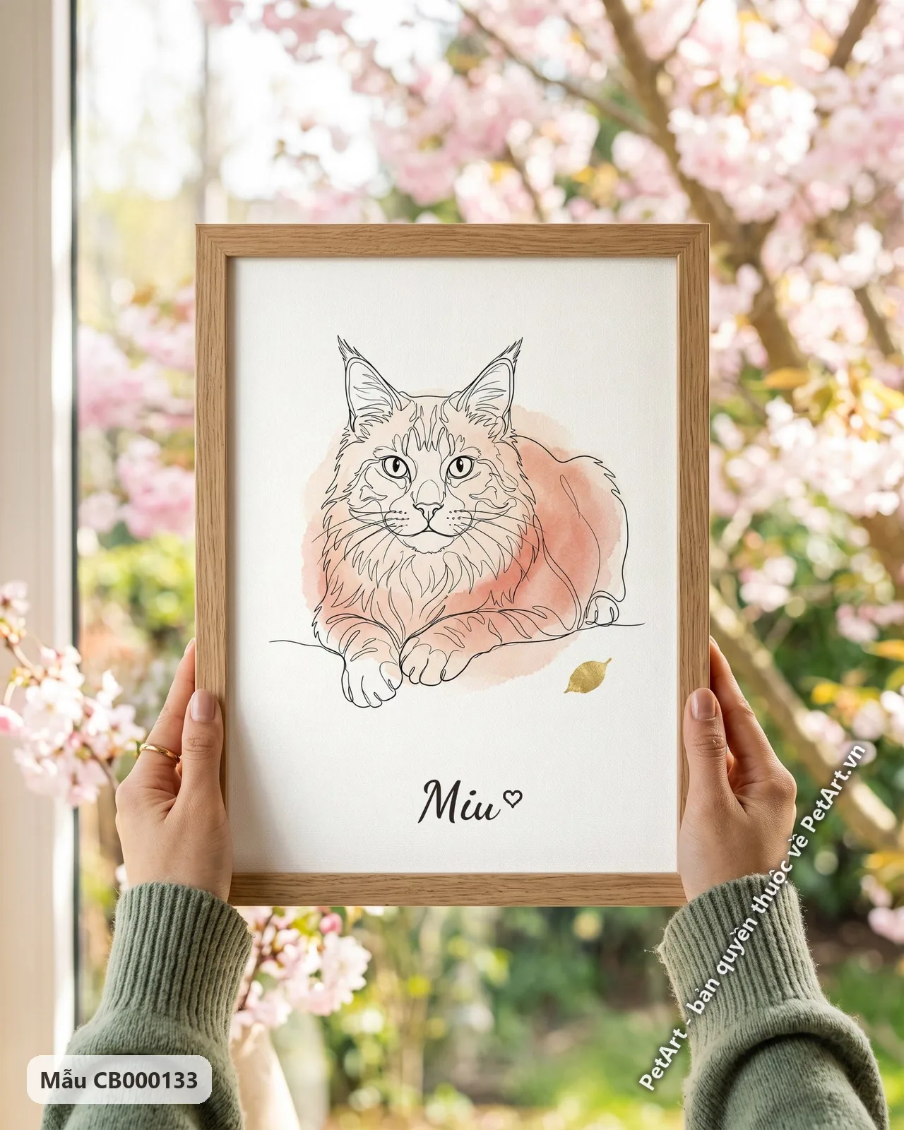 Ảnh thực tế: Mèo Maine Coon nằm thư thái, phác họa nét đen tối giản, trên nền hồng nhạt cùng chiếc lá vàng nhỏ.