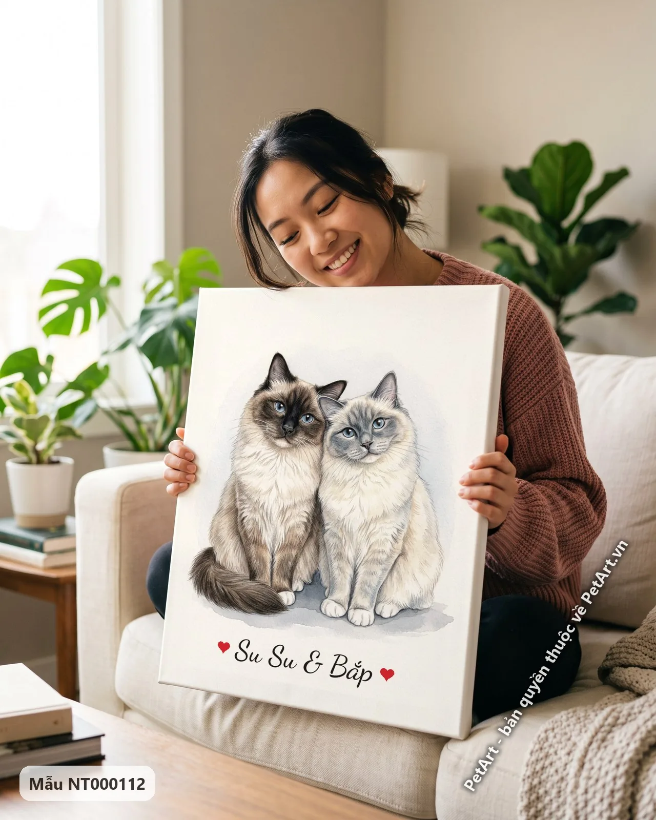 Ảnh thực tế: Bức tranh màu nước vẽ hai chú mèo Ragdoll lông dài, một màu nâu và một màu xám, đang ngồi cạnh nhau trên nền trắng đơn giản.